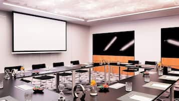 Una sala de conferencias con una larga mesa, sillas, una pantalla de proyector y una pantalla grande en la pared.