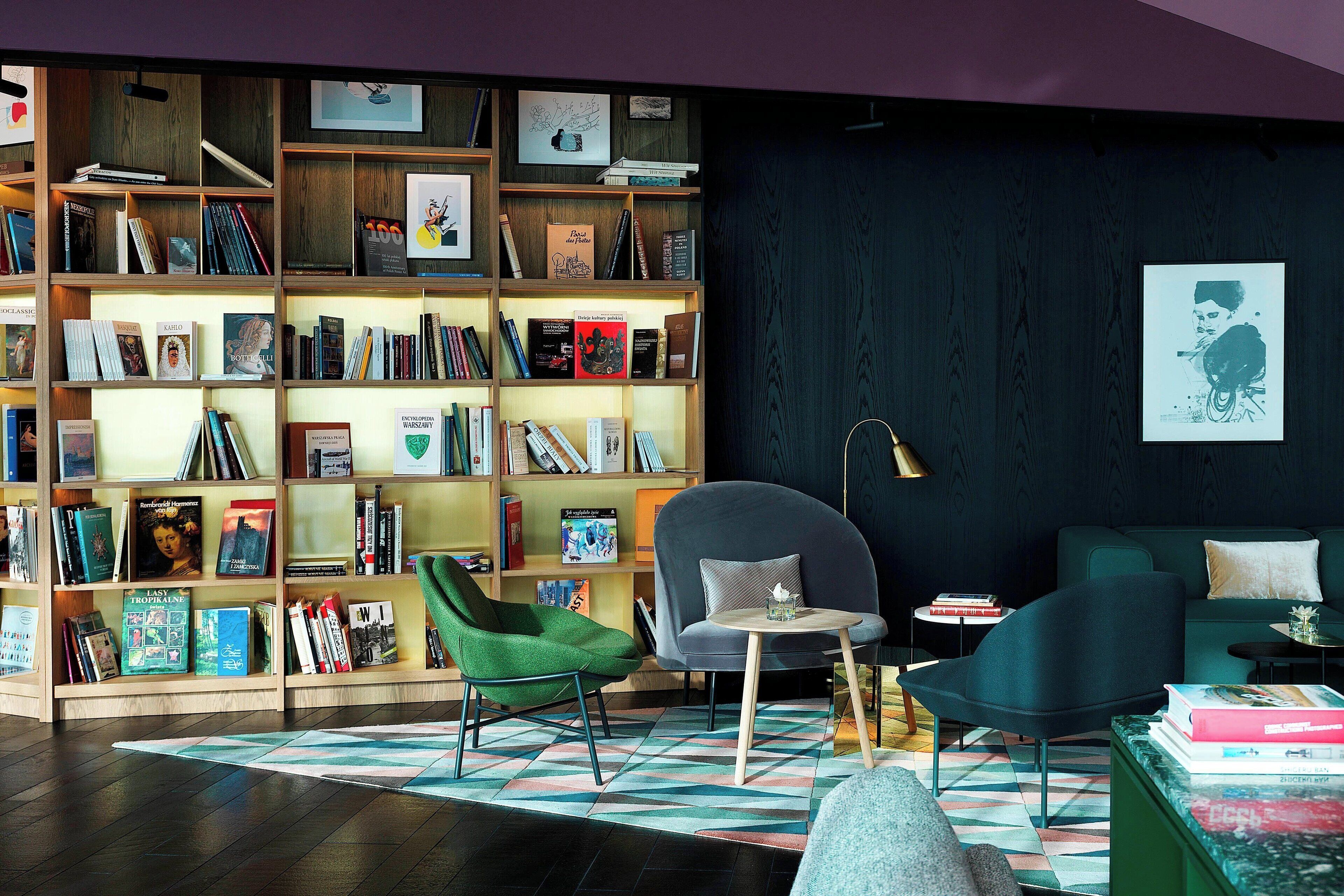 A modern living room with a large bookshelf, green armchair, and a round table with books.