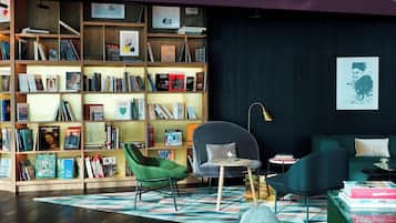 A modern living room with a large bookshelf, green armchair, and a round table with books.