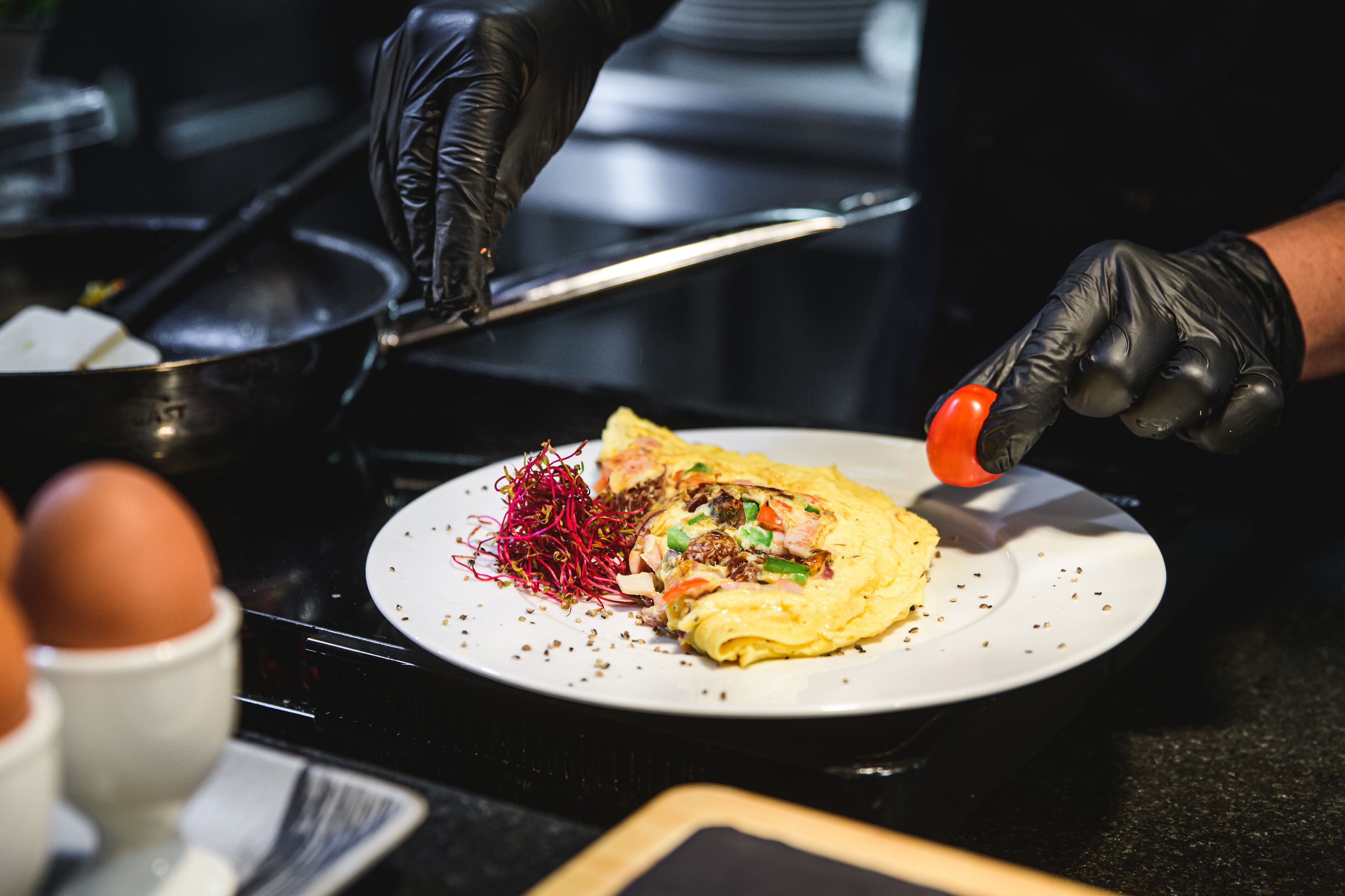 A chef preparing an omelette on a white plate with vegetables and a red garnish.