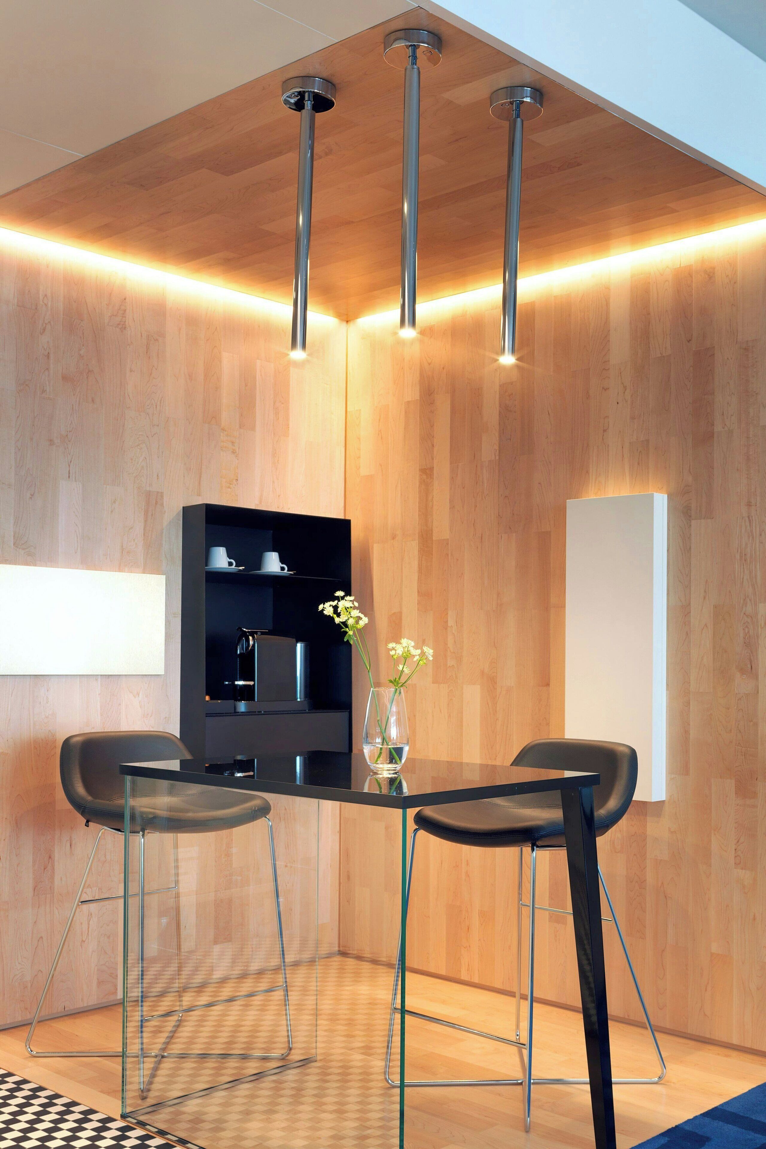 Un comedor moderno con una pared de madera, una mesa negra, dos sillas negras y un armario negro con estantes.