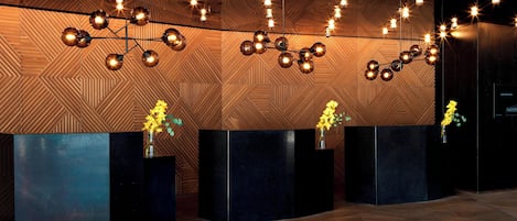 A reception area with a modern design, featuring a geometric patterned wall, a central black reception desk, and a ceiling with hanging spherical light fixtures.