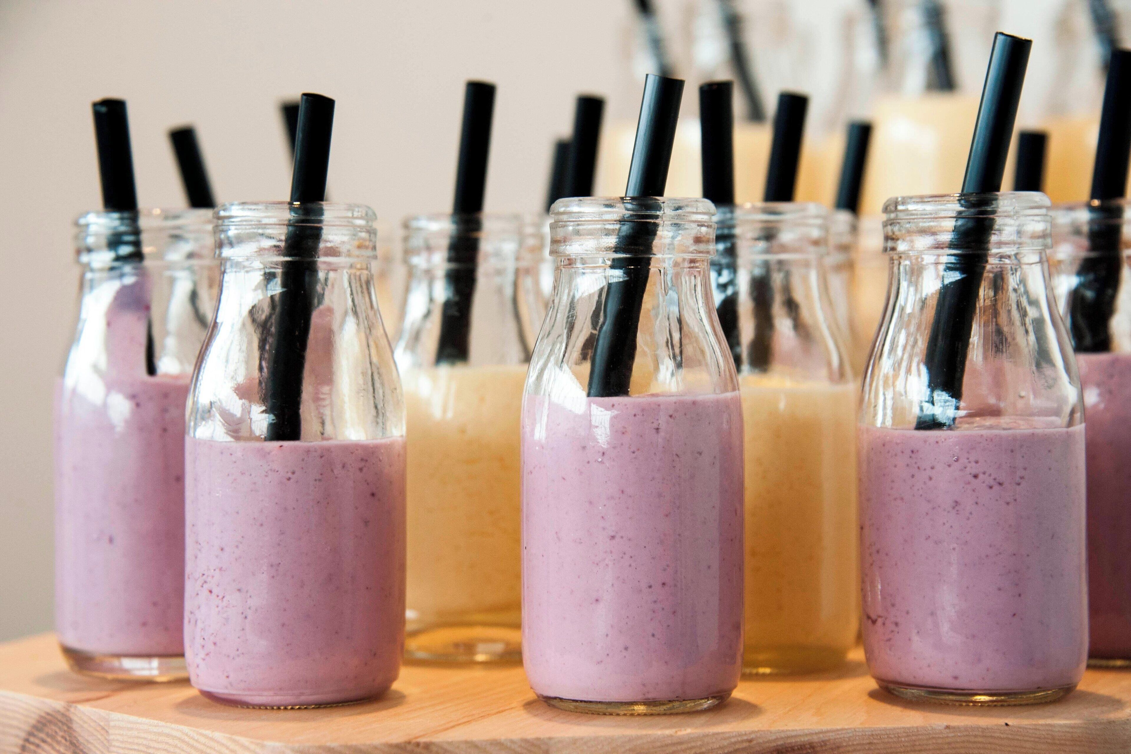 Multiple glass bottles with black straws, likely containing beverages, arranged on a wooden surface.