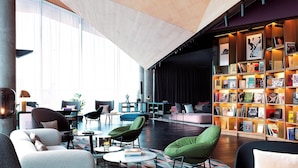 A modern lounge area with comfortable seating, a large bookshelf, and a stage. - Renaissance Warsaw Airport Hotel, an Marriott International (Warsaw)