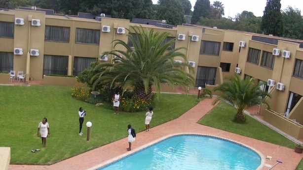 A swimming pool surrounded by a brick deck, with a building in the background featuring multiple air conditioning units. - Welkom INN (Welkom)