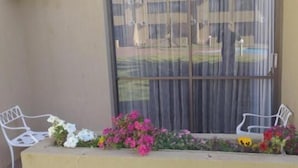 A balcony with two white chairs, a variety of flowers, and a view of a building through a window. - Welkom INN (Welkom)
