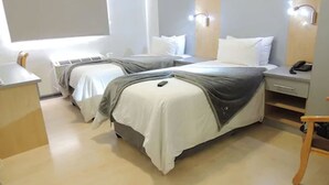 A hotel room with two beds, a desk, a chair, and a bedside table with a phone. - The Gallagher Hotel (Midrand)