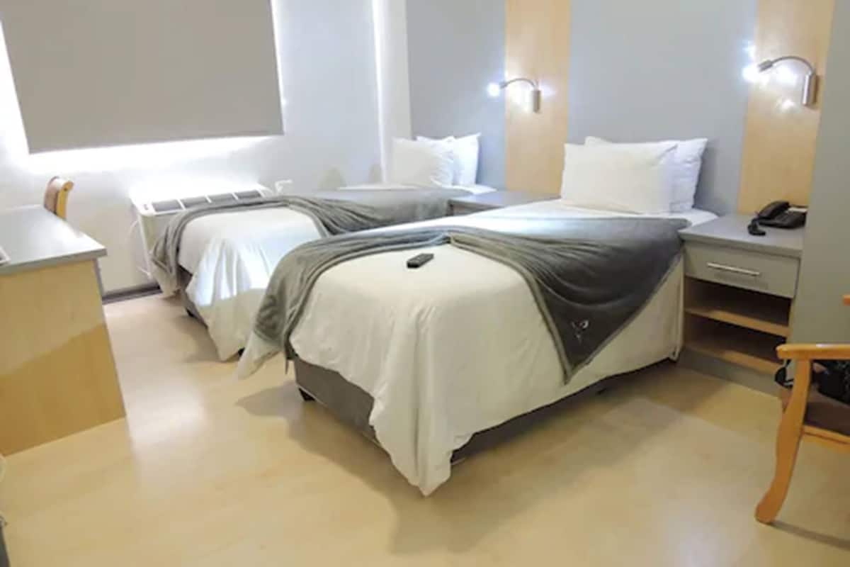 Habitación de hotel con dos camas, un escritorio, una silla y una mesita de noche con teléfono.