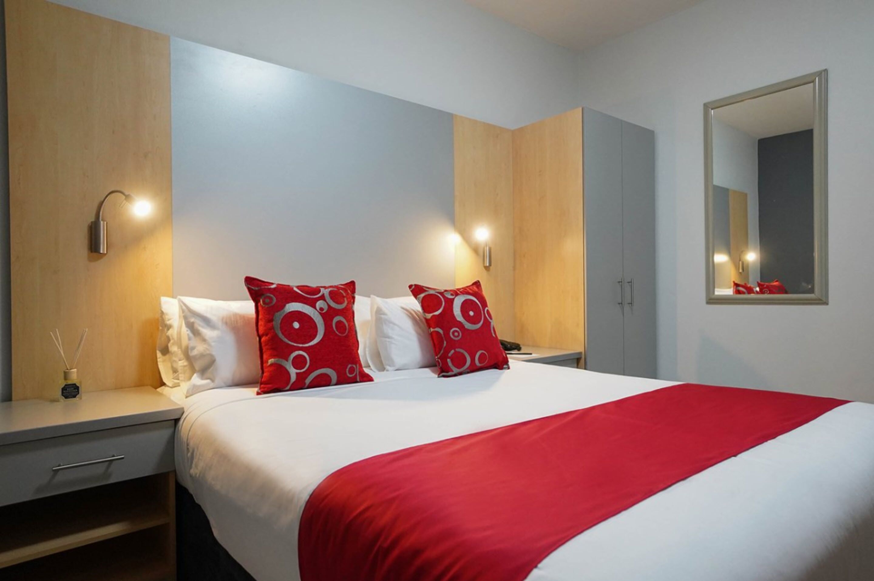 Een hotelkamer met een groot bed, twee nachtkastjes, een spiegel en een kledingkast.