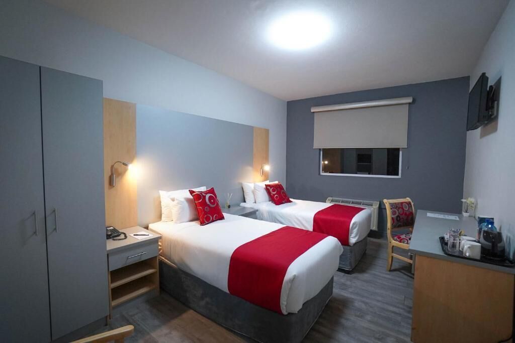 A hotel room with two beds, a desk, a chair, a wardrobe, and a window with a blind.