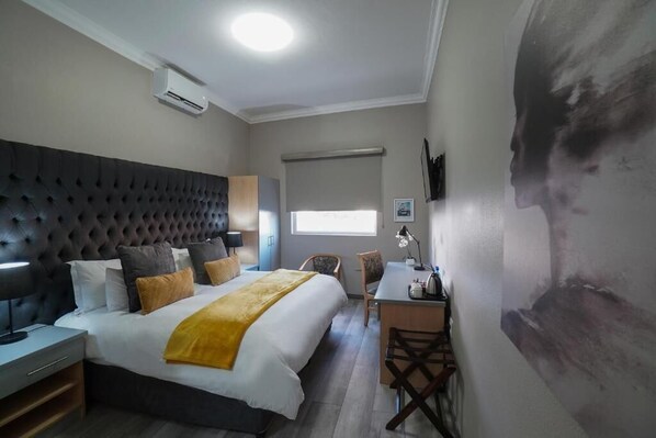 Una camera d'albergo con un letto dotato di testiera capitonata, una scrivania con una sedia, un condizionatore d'aria e un'ampia finestra.