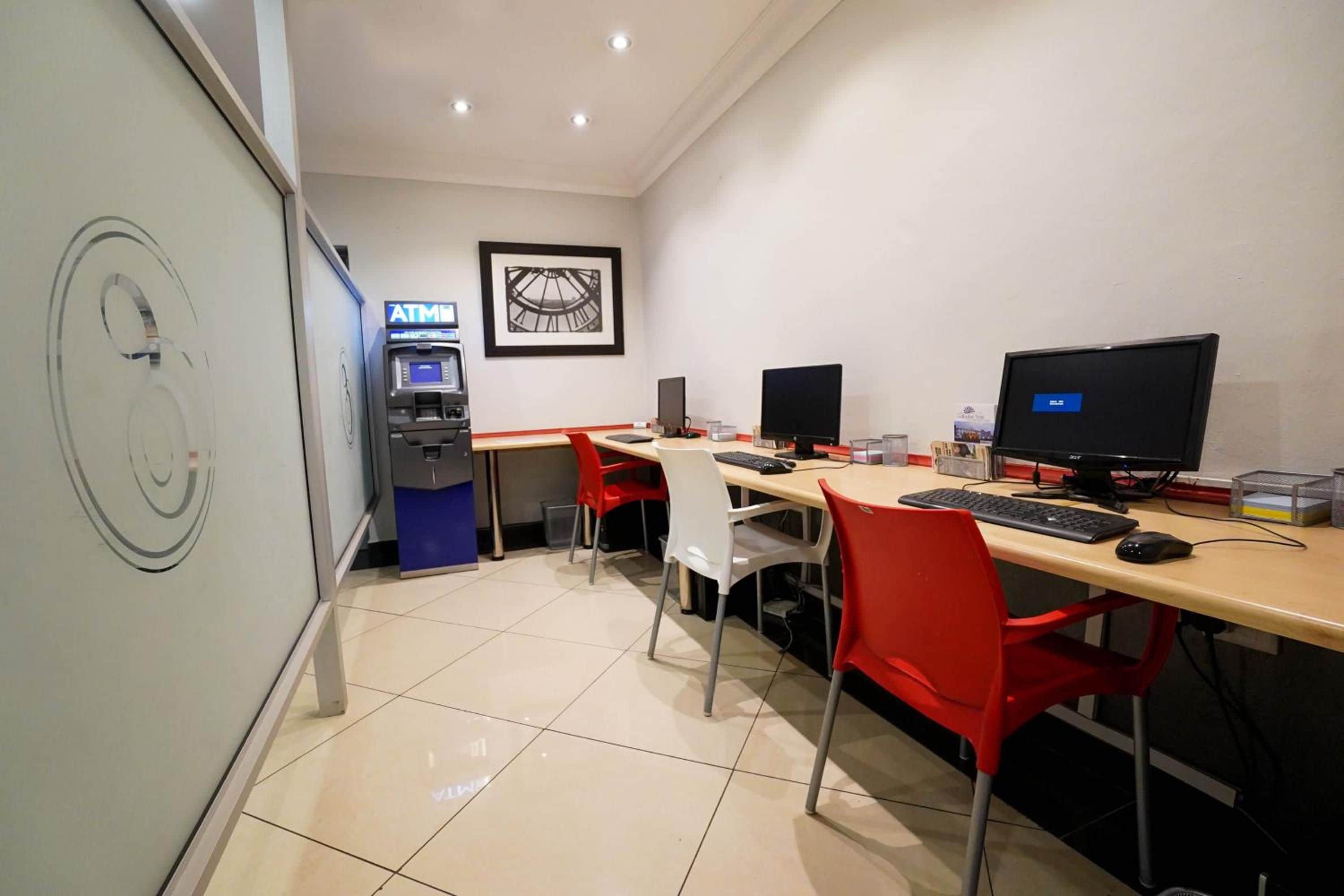 A modern office space with a desk, chairs, computers, and an ATM machine.