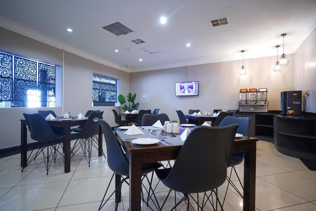 A hotel dining area with multiple tables and chairs, a television screen, and a coffee machine.