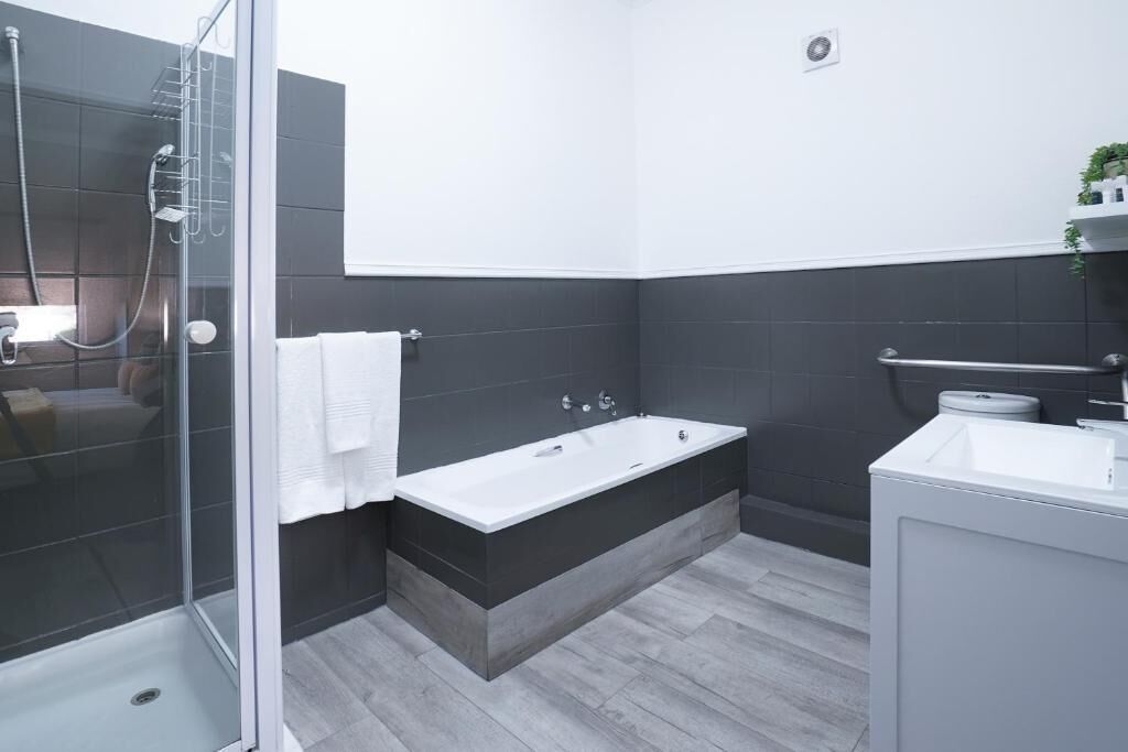 A modern bathroom with a glass shower enclosure, a freestanding bathtub, and a white sink.