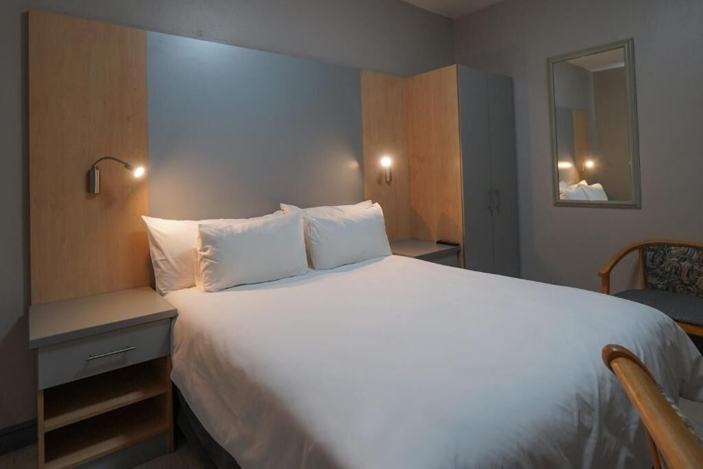 Une chambre d’hôtel avec un lit, des tables de chevet, une chaise et un miroir.