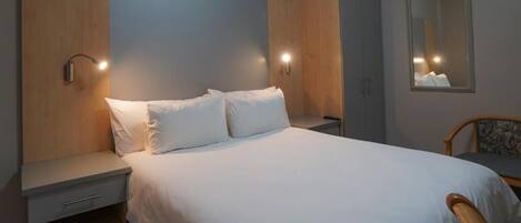 Une chambre d’hôtel avec un lit, des tables de chevet, une chaise et un miroir.