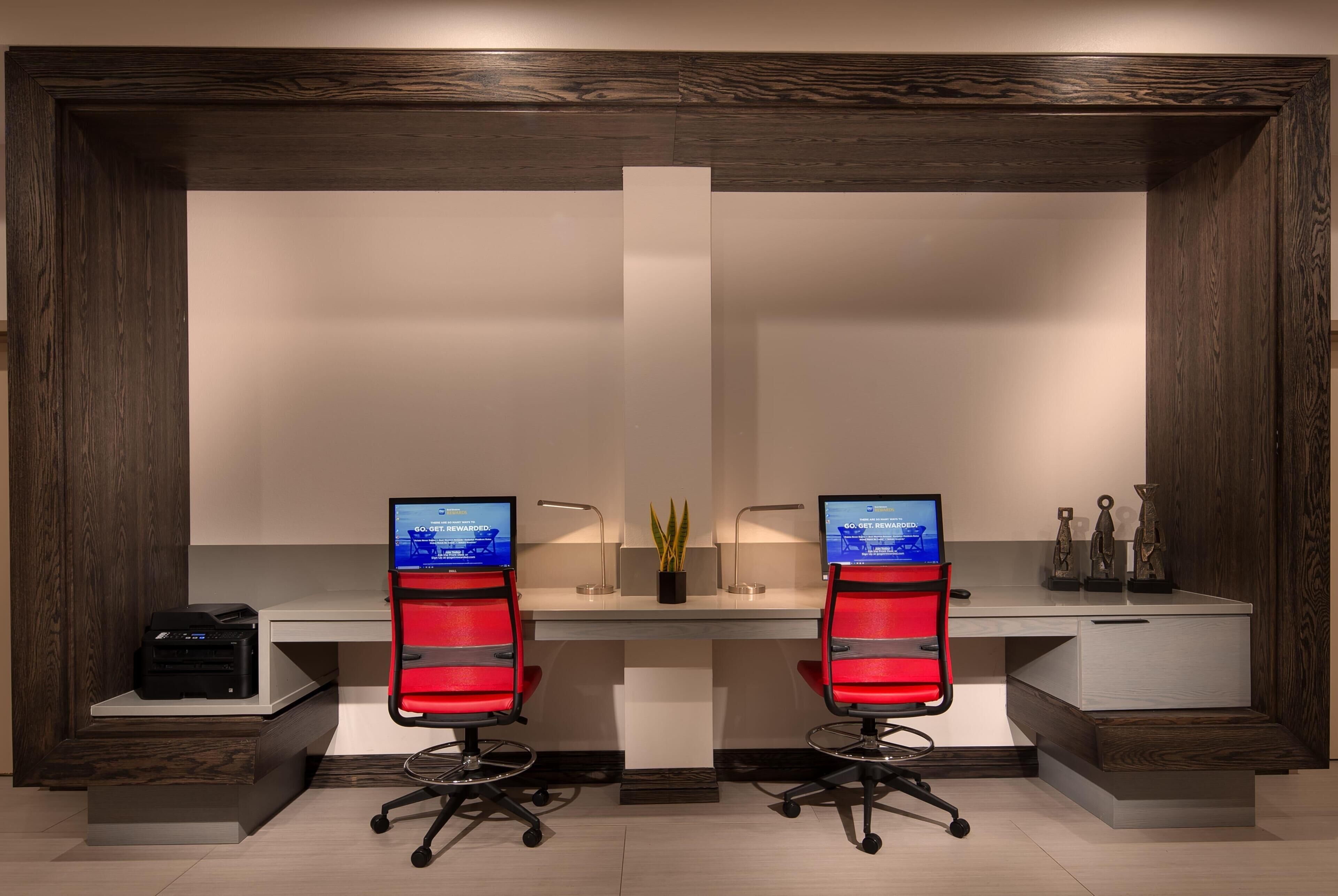 A modern office desk with two red chairs, a printer, and decorative items.