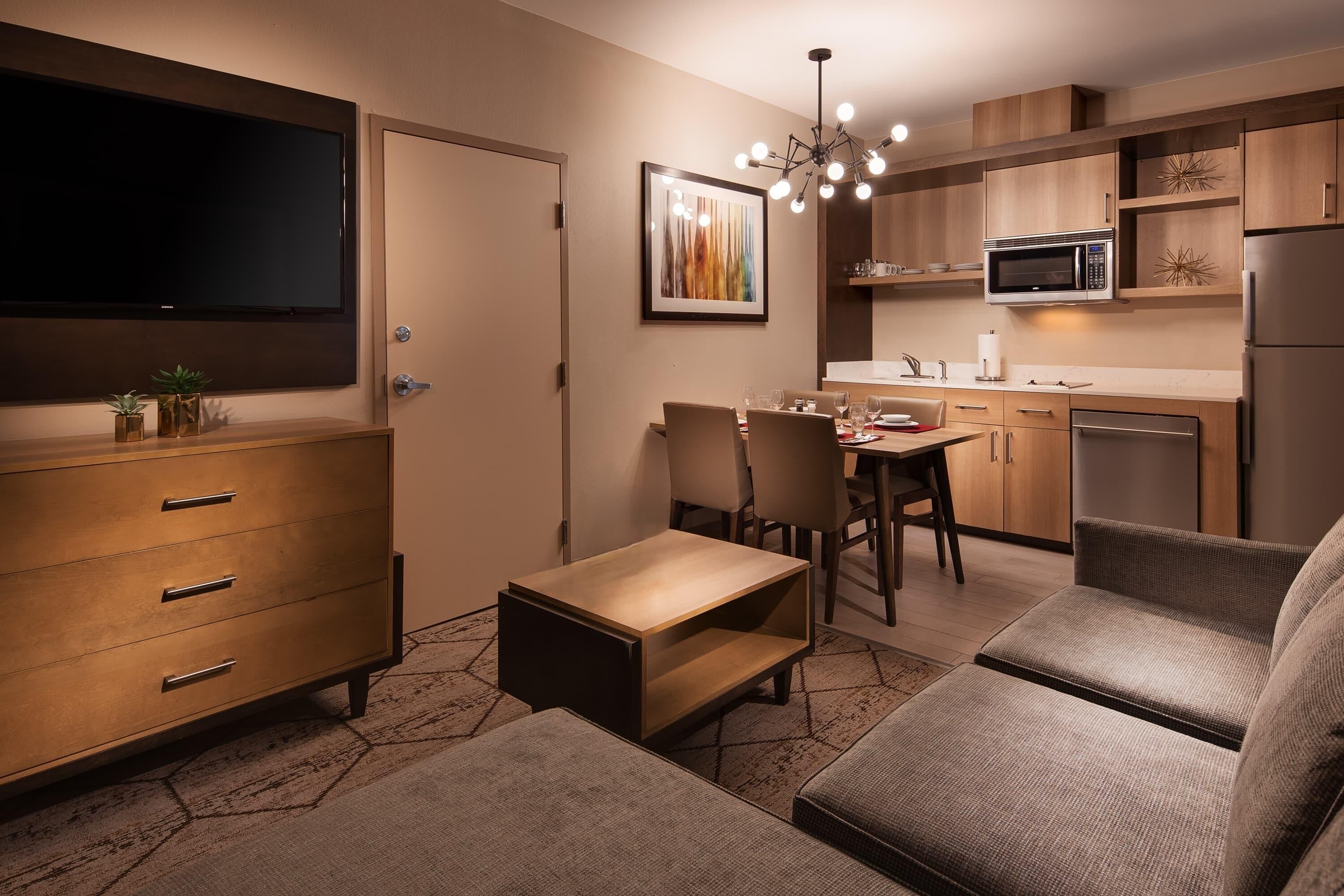 Ett kompakt bostadsutrymme med TV, matplats, litet kök och sittmöbler.