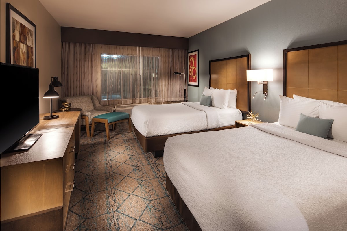 Une chambre d’hôtel avec deux lits, un bureau, une chaise, une télévision et une fenêtre avec des rideaux.
