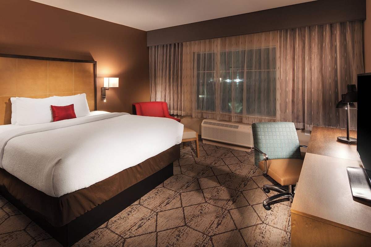 Une chambre d’hôtel avec un grand lit, un bureau avec une chaise, une télévision et une fenêtre avec des rideaux.