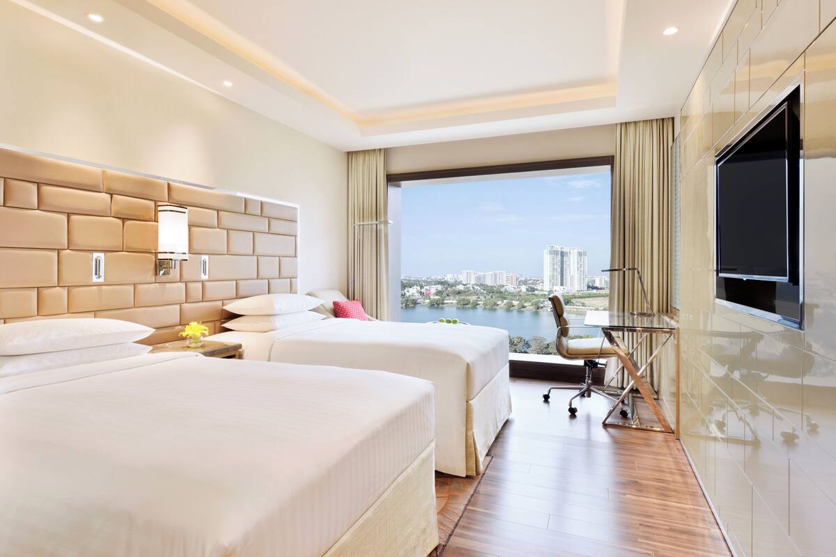 Une chambre d’hôtel avec deux lits, un bureau, une chaise, une télévision et une vue sur le paysage urbain.