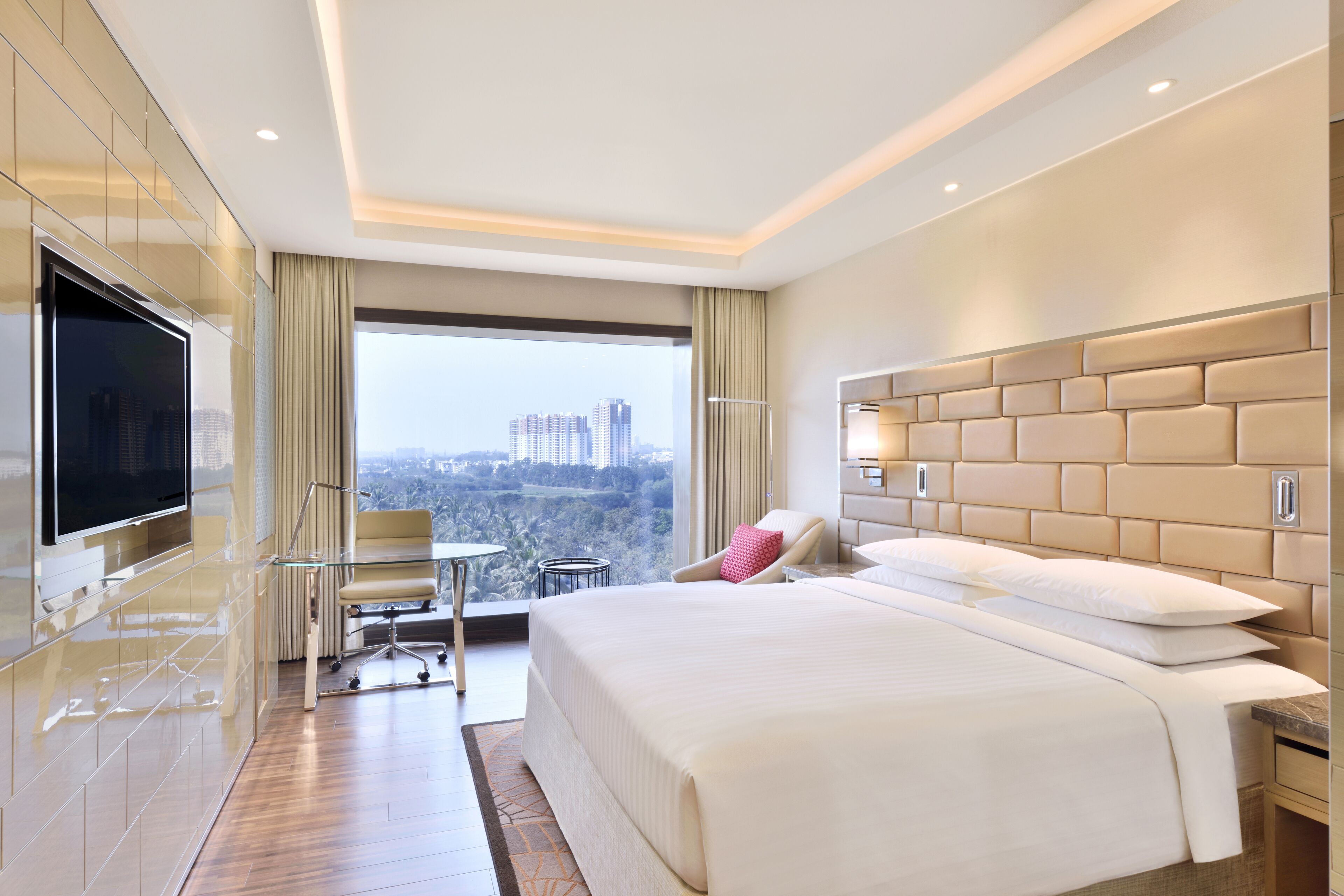 A modern hotel room with a large bed, a TV, a desk, and a view of the city.