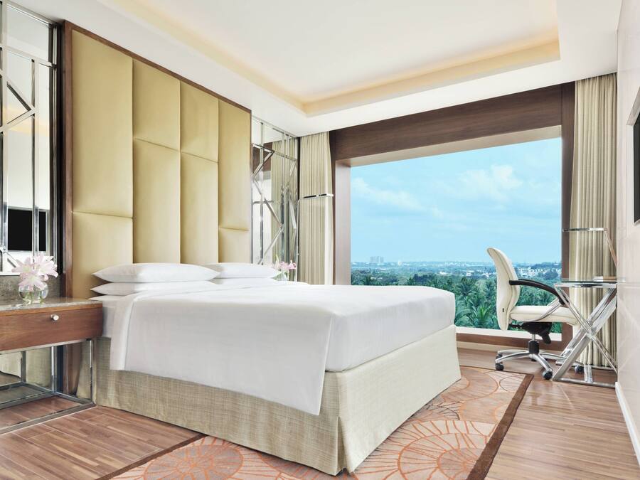 A modern hotel room with a large bed, a desk, a chair, and a view of the city.