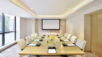 A conference room with a long table, chairs, a projector screen, and a large window.