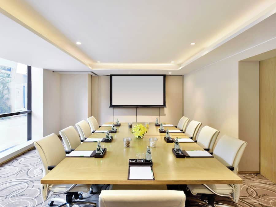 A conference room with a long table, chairs, a projector screen, and a large window.