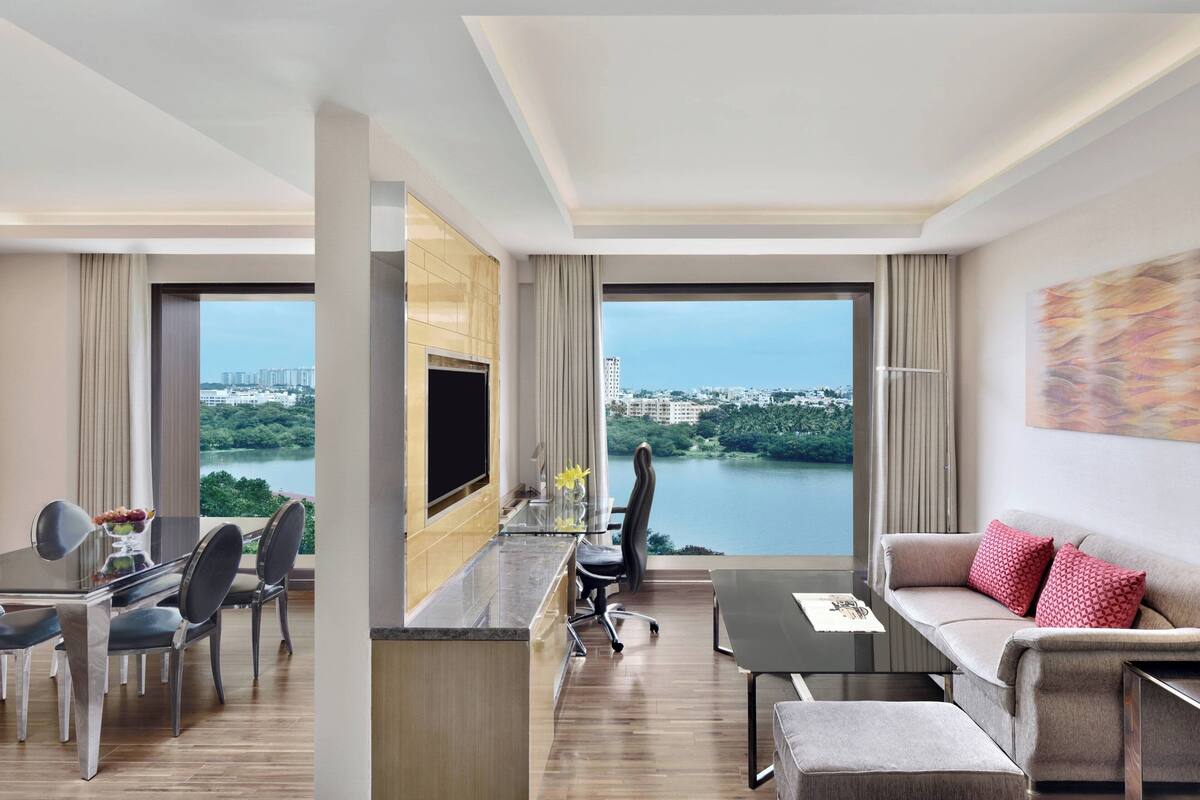 Une chambre d’hôtel moderne dotée d’un coin repas, d’un canapé et offrant une vue sur un lac et le paysage urbain.