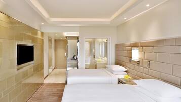 A hotel room with two beds, a TV, a mirror, and a bathroom visible through a glass door.