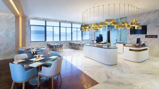Un hall d’hôtel moderne avec un sol en marbre, un comptoir d’accueil, un espace salon et de grandes fenêtres offrant une vue panoramique.