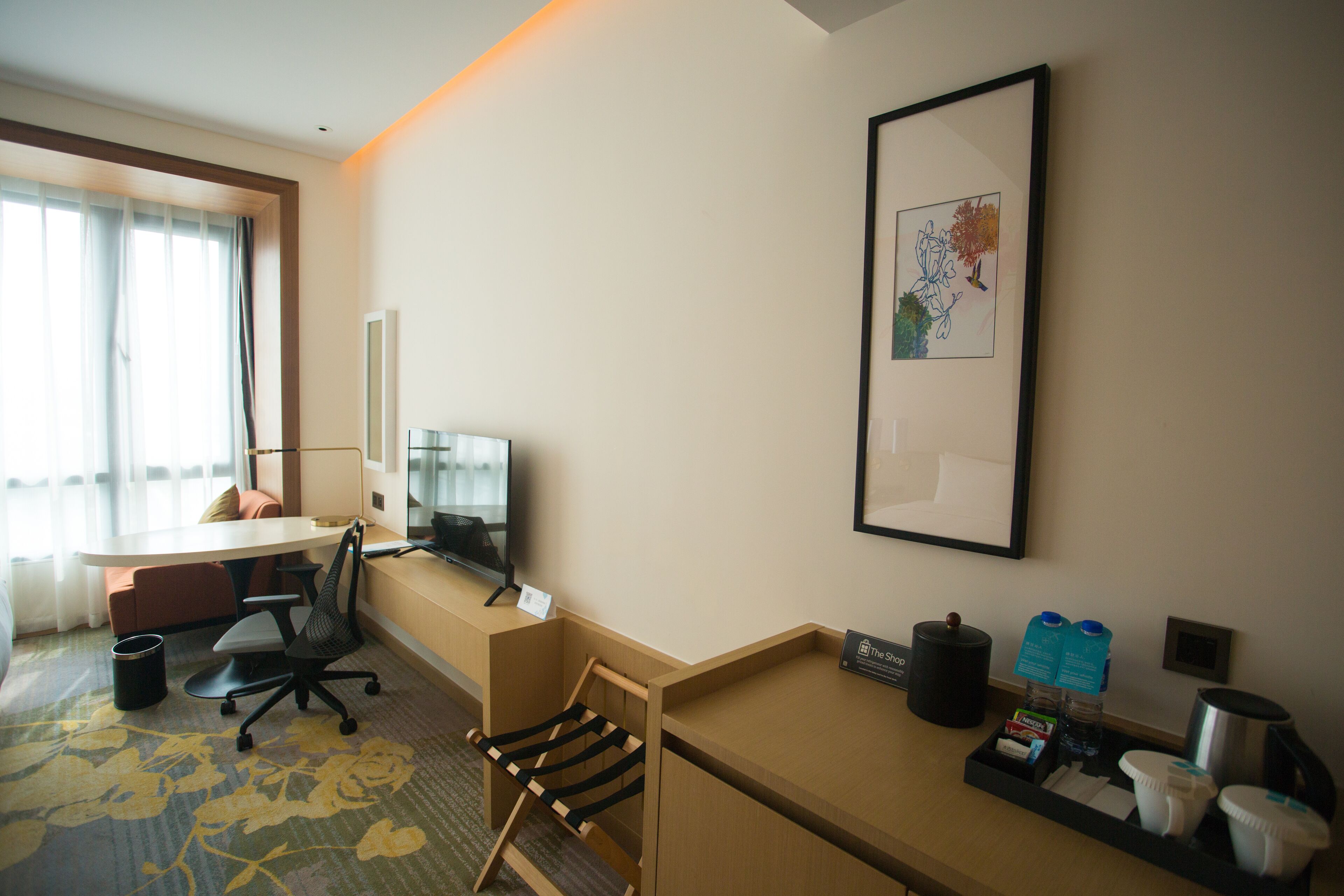 A hotel room with a desk, chair, television, and a coffee station.