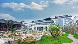 Un hôtel de style architectural chinois traditionnel, un bâtiment moderne et un jardin aménagé avec un étang.
