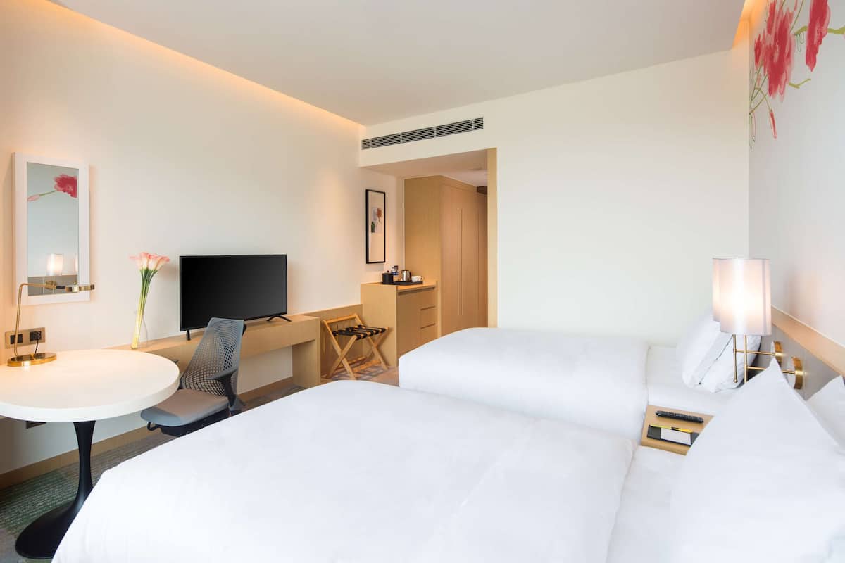 A hotel room with two beds, a desk with a chair, a TV, a small table, and a lamp.