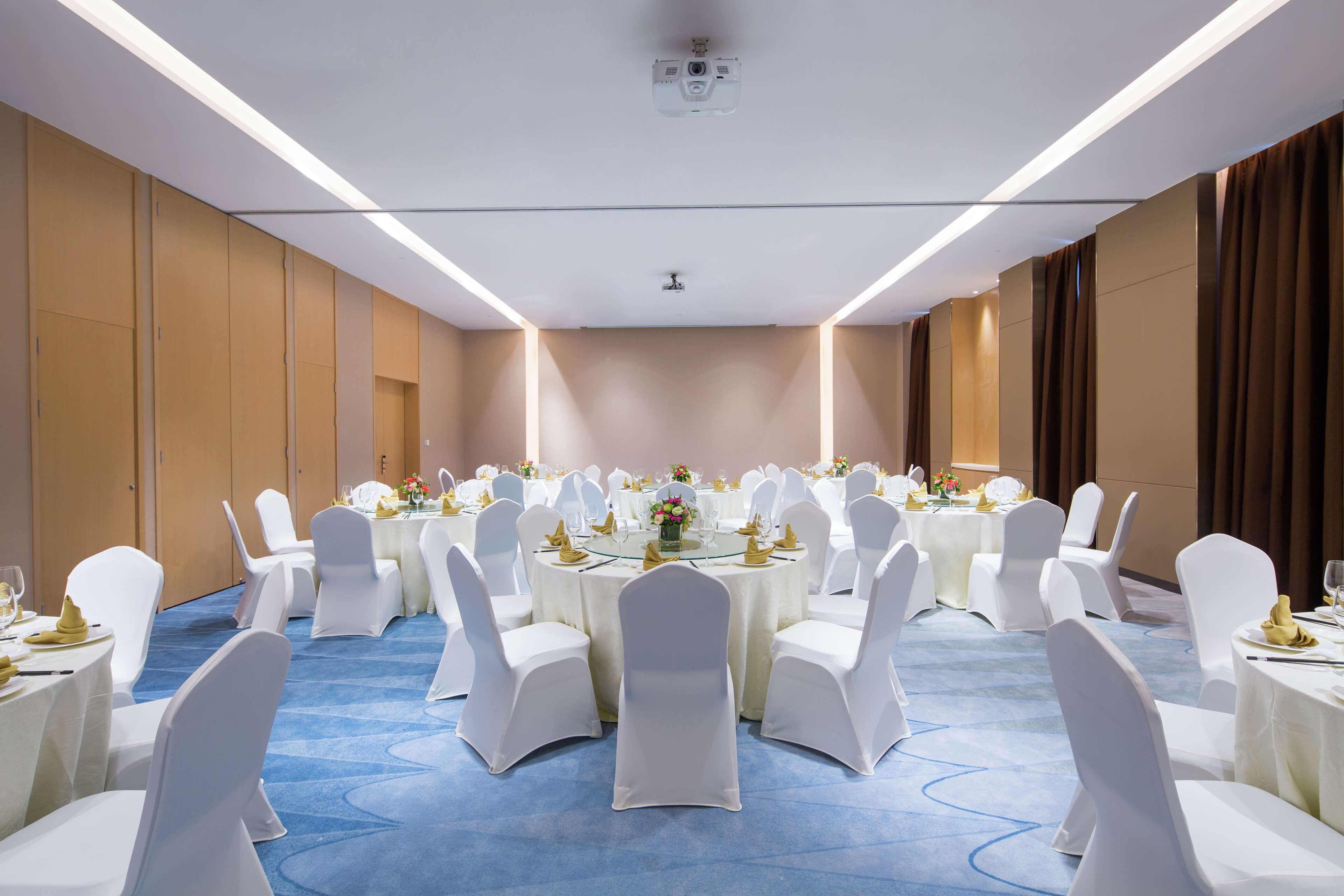A conference room with round tables, white chairs, and blue carpeting.