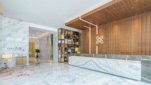 Un espace d’accueil moderne avec un sol en marbre, un comptoir d’accueil en bois et une plante.