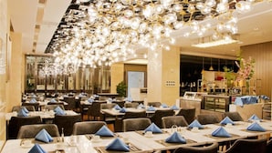 A spacious restaurant with multiple tables set for dining, featuring a modern chandelier and a bar area in the background. - Howard Johnson Life Geckor Zhu (Zhuzhou)