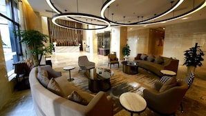 A modern lobby with a curved sofa, round tables, and a reception desk. - Howard Johnson Life Geckor Zhu (Zhuzhou)