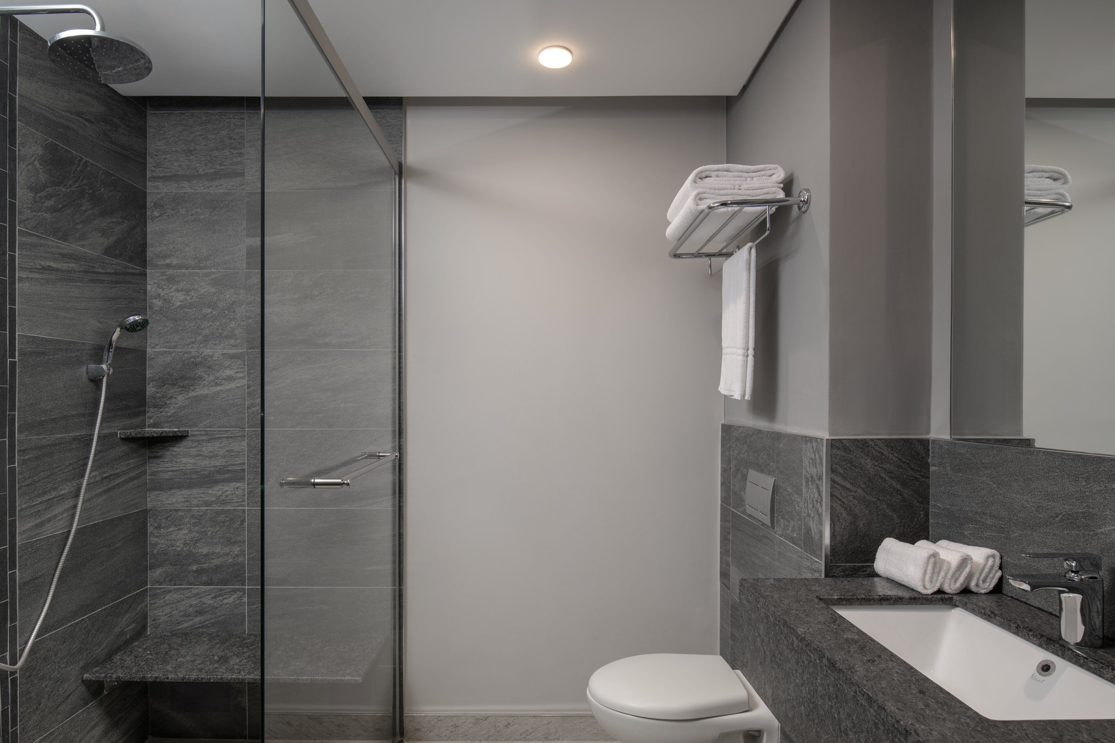 A modern bathroom with a glass-enclosed shower, a white toilet, and a marble countertop with a sink and towel rack.