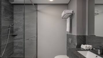 A modern bathroom with a glass-enclosed shower, a white toilet, and a marble countertop with a sink and towel rack.