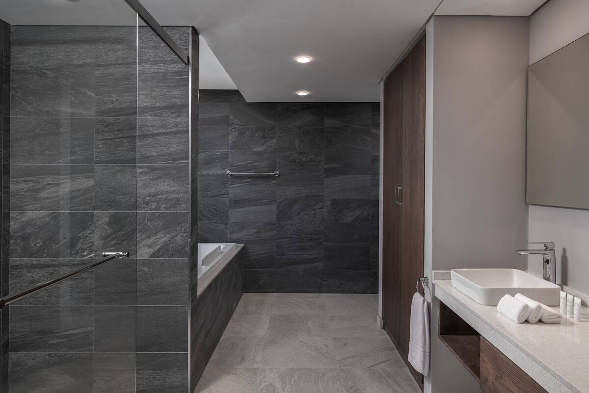 A modern bathroom with dark tiles, a glass shower enclosure, a bathtub, and a vanity with a mirror.
