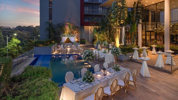 A rooftop pool area with tables set for dining, surrounded by lush greenery and palm trees. - Holiday Inn Nairobi Two Rivers Mall by IHG (Nairobi)