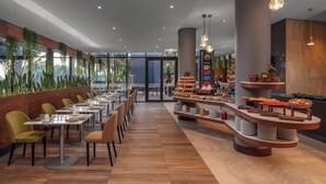 A modern restaurant with long tables and chairs, a buffet area with various food items, and a view of the outdoors through large windows. - Holiday Inn Nairobi Two Rivers Mall by IHG (Nairobi)