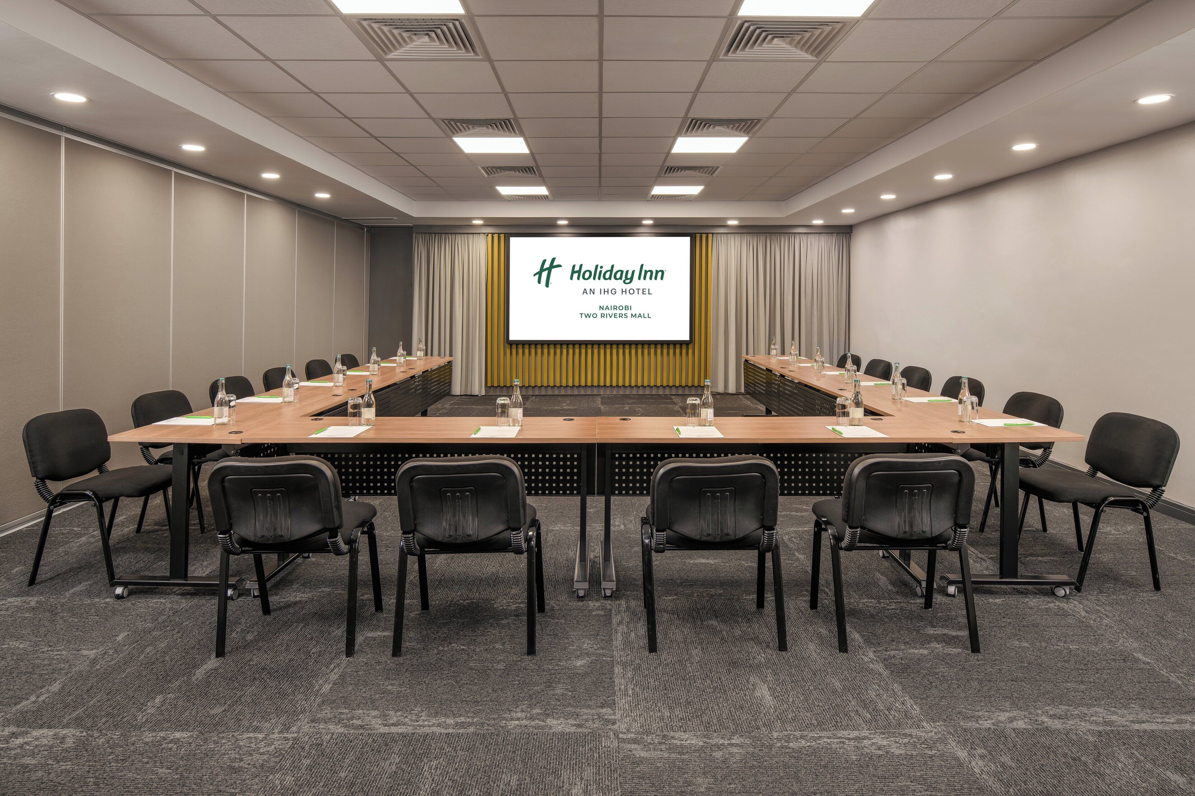A conference room with a long table, chairs, and a screen displaying the Holiday Inn logo.