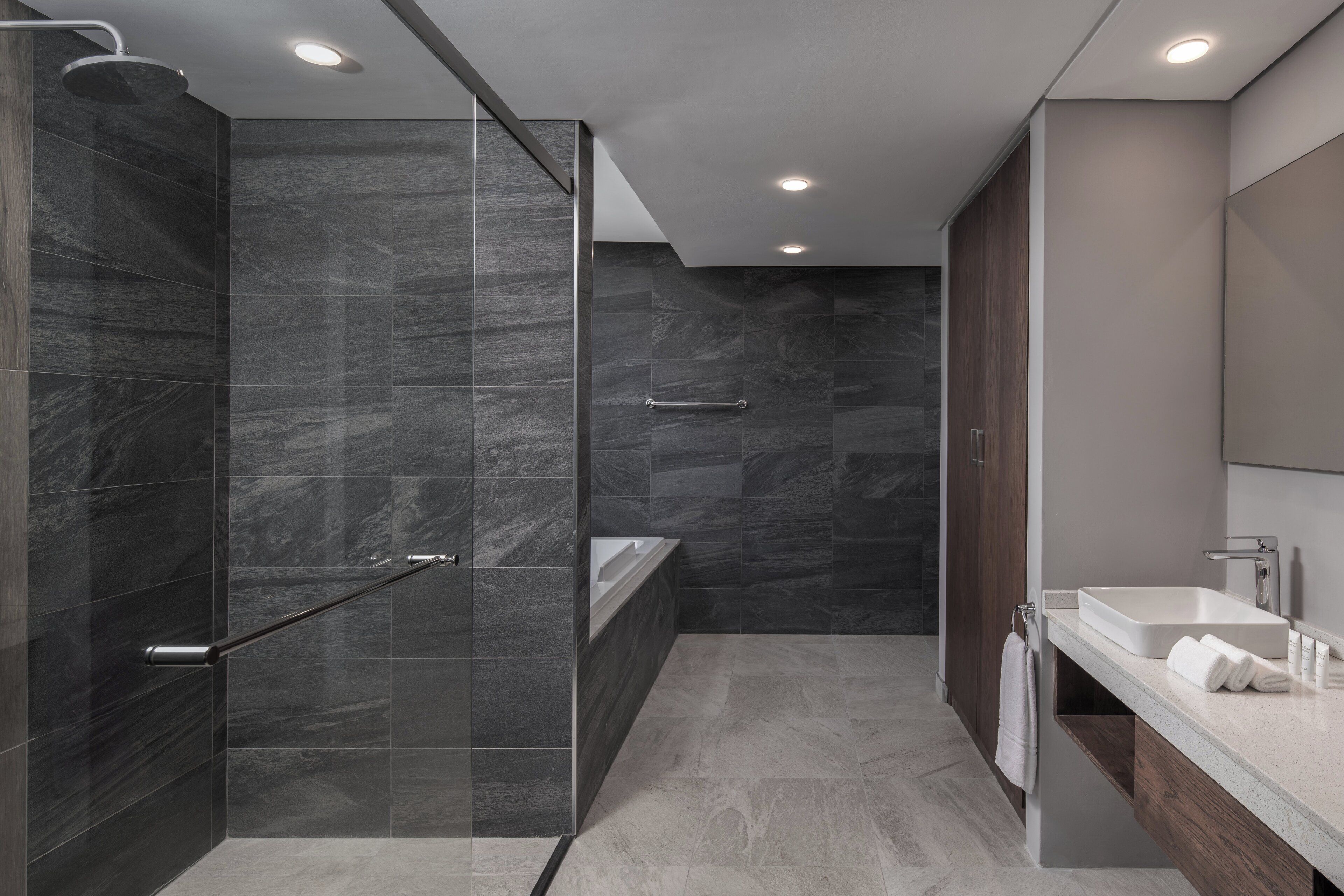 A modern bathroom with a glass-enclosed shower, a bathtub, and a vanity with a mirror.
