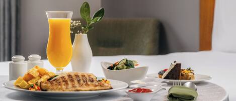 A breakfast setting with a plate of food, a glass of orange juice, a bowl of salad, and a small dish of ketchup.