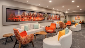 A modern lobby with a cityscape painting, a white sofa, orange and white armchairs, and a wooden coffee table. - Holiday Inn Nairobi Two Rivers Mall by IHG (Nairobi)