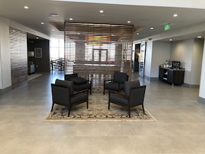 Eine geräumige Lobby mit modernem Design, ausgestattet mit einer Sitzecke mit dunklen Stühlen und einem gemusterten Teppich, einem Empfangstresen und einer dekorativen Holzvertäfelung.