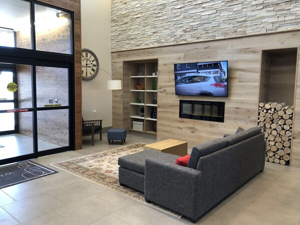Ein modernes Wohnzimmer mit einem grauen Sofa, einem Couchtisch und einem an einer Steinwand montierten Fernseher. Unter dem Fernseher befindet sich ein Bücherregal und ein Kamin.